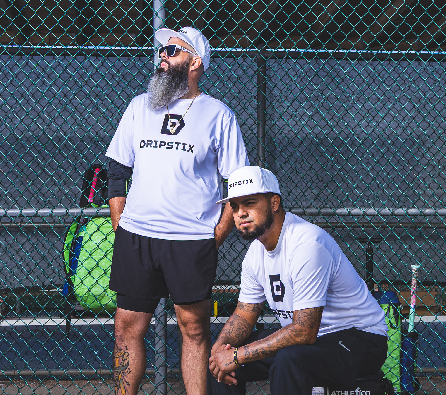 Two men on a tennis court wearing Dripstix branded shirts and hats.